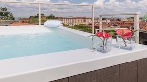 Una piscina en la azotea con borde blanco, dos jarrones de vidrio con flores rosadas y una toalla blanca.