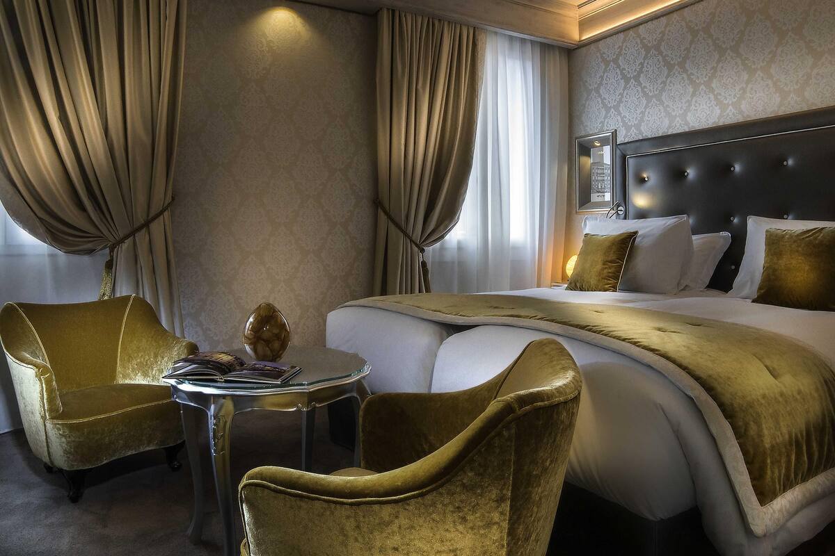 A hotel room with a large bed, two armchairs, a small table, and a mirror on the wall.