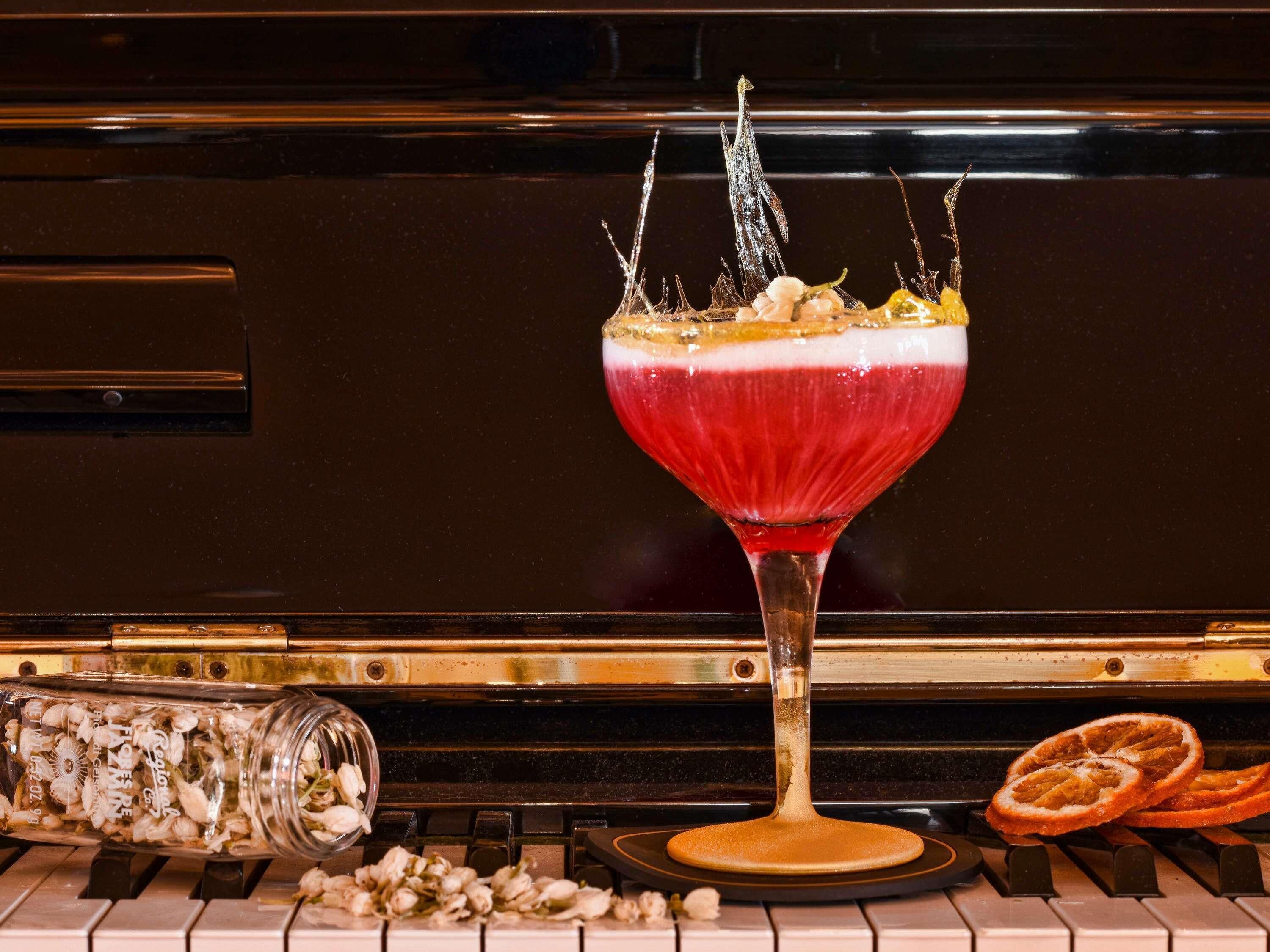 A cocktail glass with a red drink, ice, and a garnish on a piano keys background.
