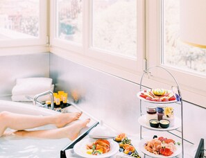 A spa setting with a hot tub, a three-tiered serving cart with food and drinks, and a view of the outdoors through large windows. - Papadopoli Hotel Venezia - MGallery Collection (Venice)