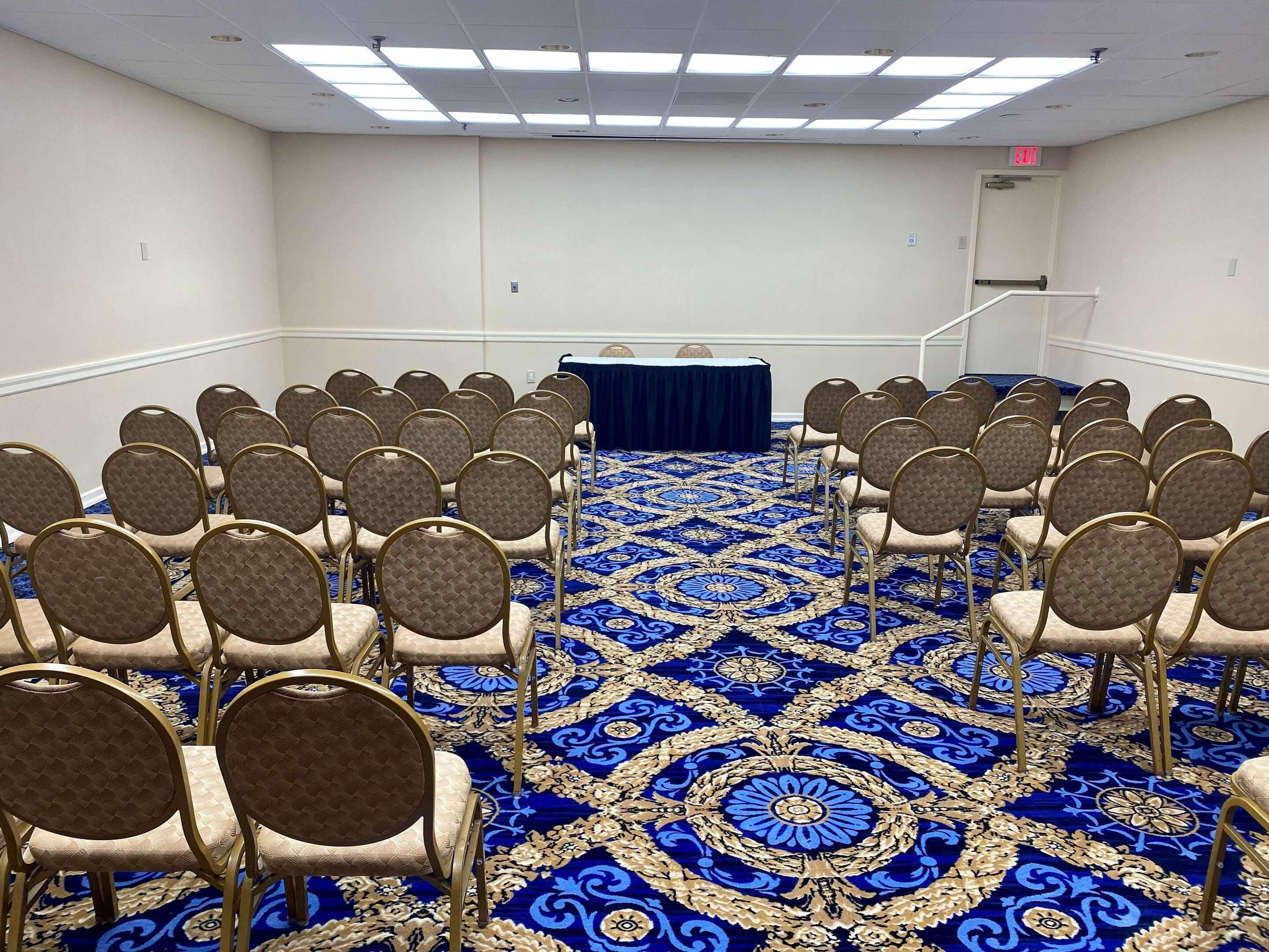 A conference room with rows of chairs, a blue carpet, and a table with a dark cloth.