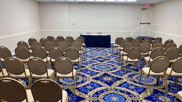 A conference room with rows of chairs, a blue carpet, and a table with a dark cloth.
