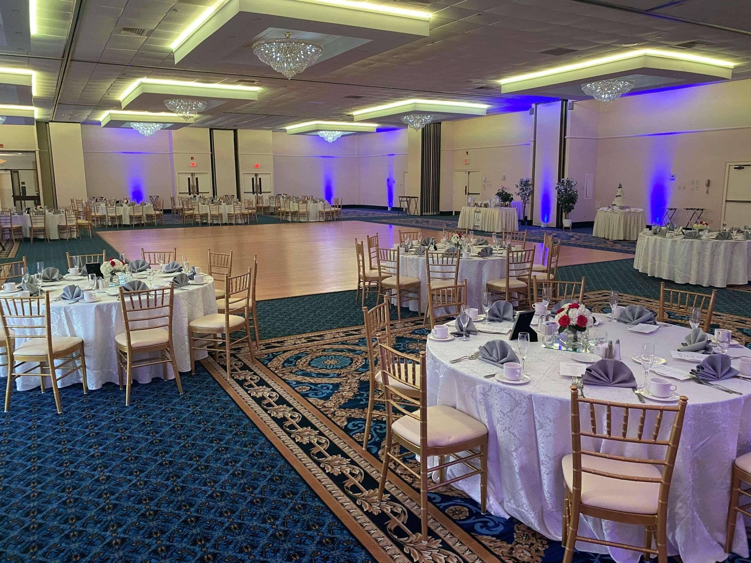 A banquet hall with round tables and chairs, a dance floor, and a carpeted floor.