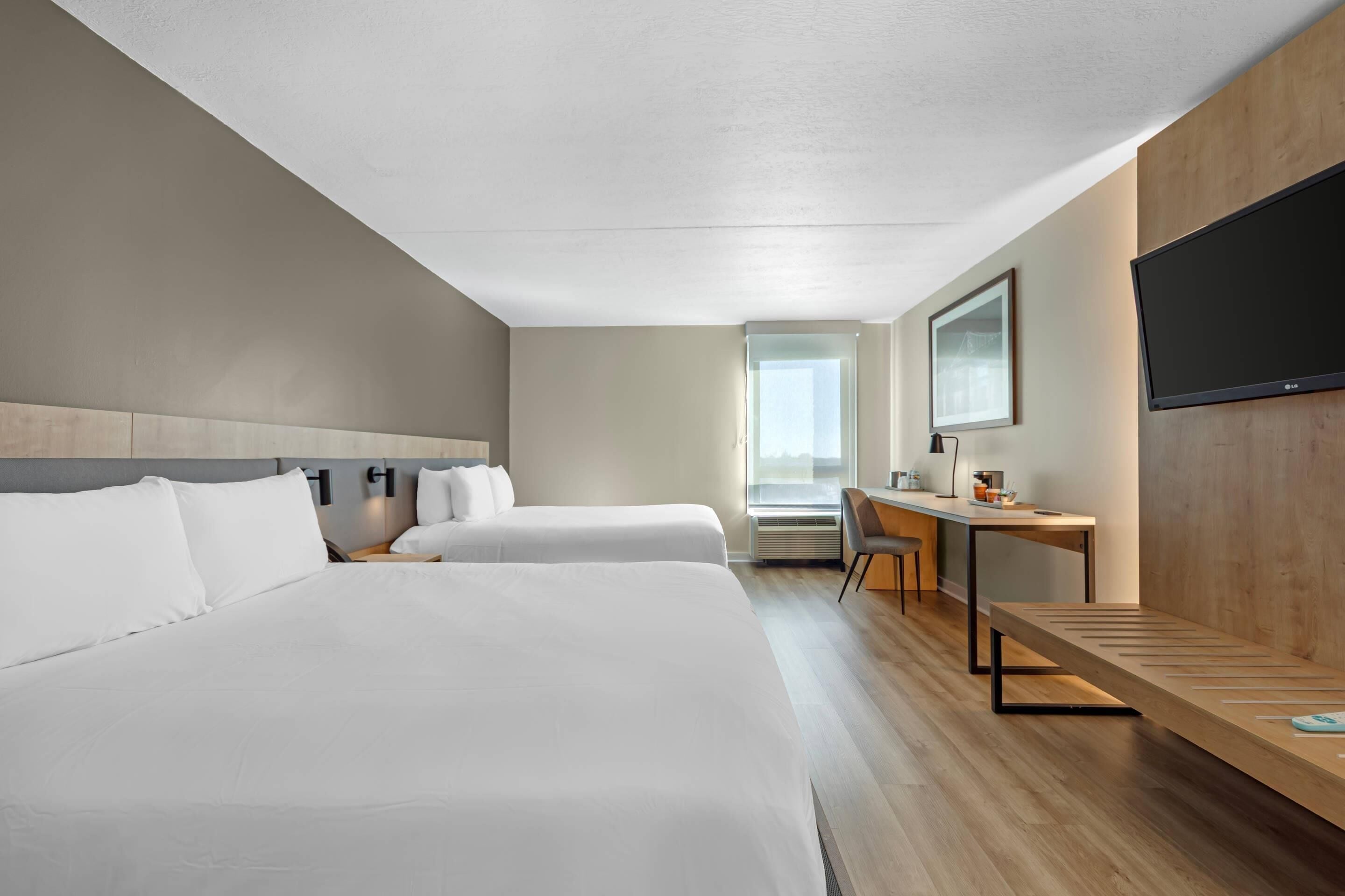 Ein Hotelzimmer mit zwei Betten, einem Schreibtisch, einem Stuhl, einem Fernseher und einem Fenster.