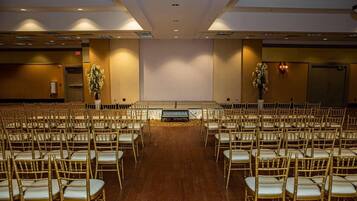 A conference room with rows of golden chairs, a stage at the front, and a large wall with a floral arrangement.