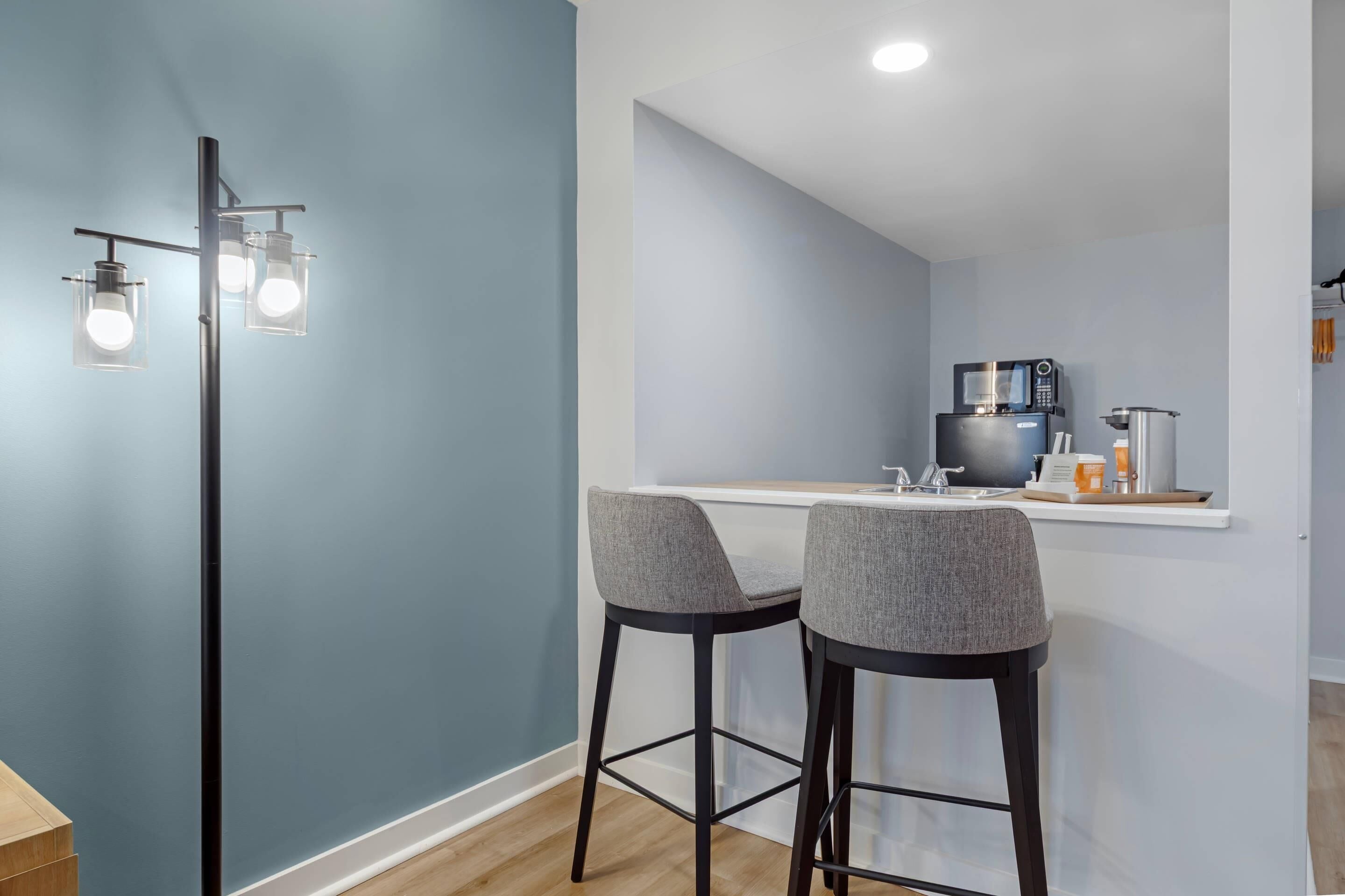 A modern kitchen with a white countertop, two bar stools, and a microwave.