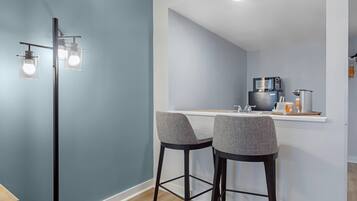 A modern kitchen with a white countertop, two bar stools, and a microwave.