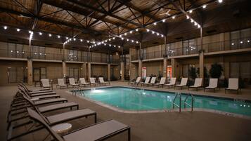 An indoor swimming pool with lounge chairs and a ceiling with exposed beams and string lights.