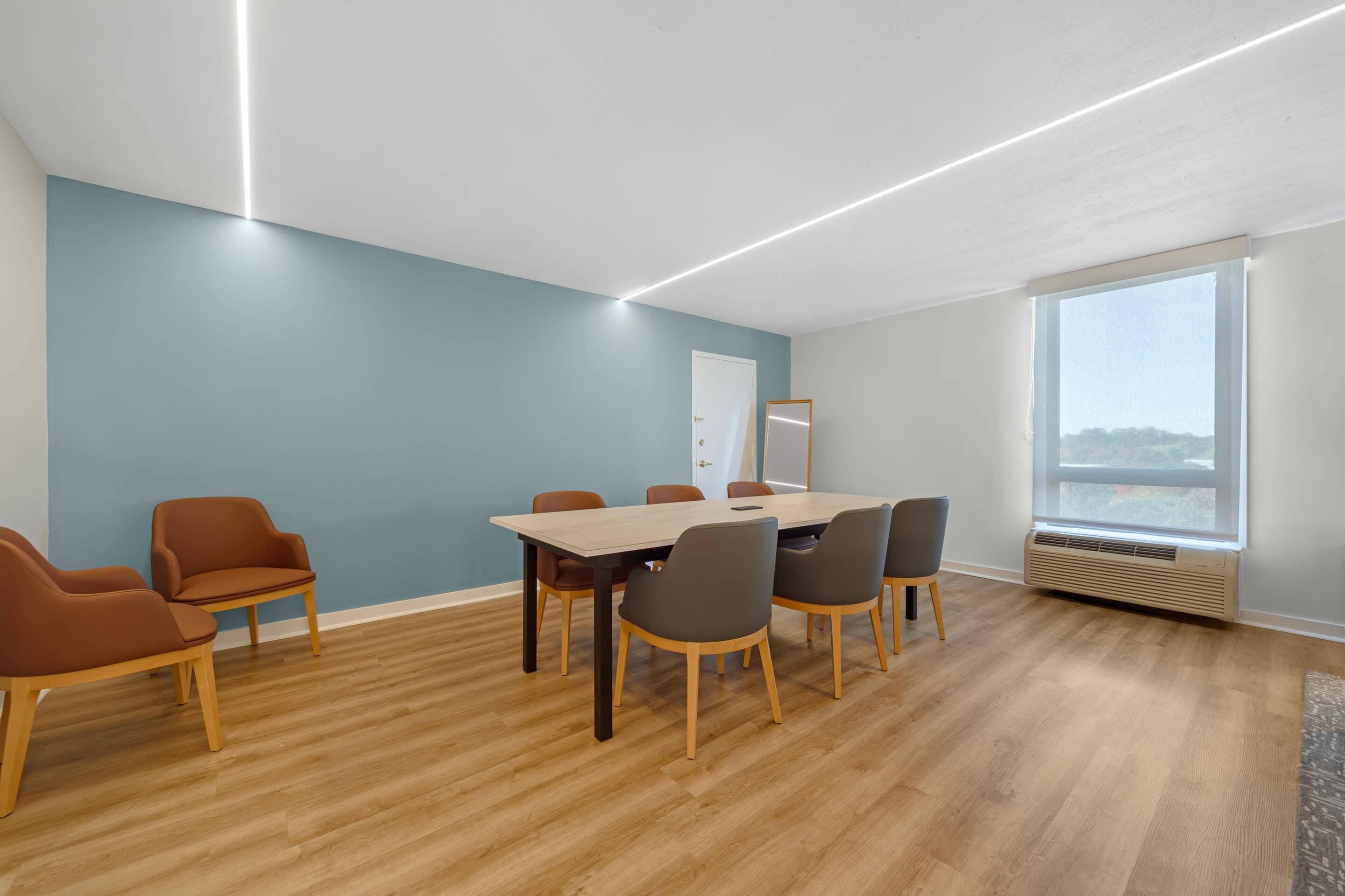 A conference room with a wooden table, six chairs, and a whiteboard.