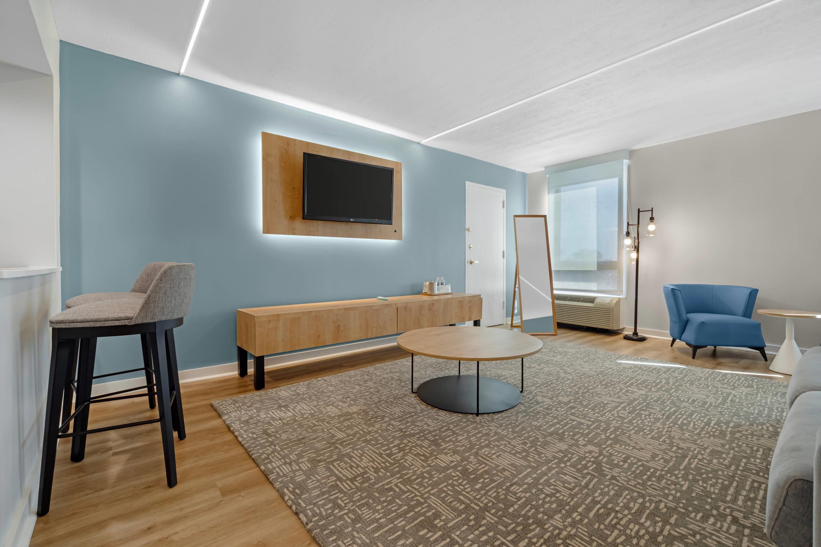 Een moderne woonkamer met een blauwe wand, een houten bankje, een ronde salontafel, een blauwe fauteuil en een staande lamp.