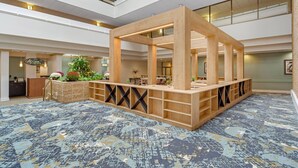 A spacious lobby with a central wooden structure, a patterned carpet, and a reception desk with a plant.