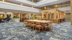 A spacious lobby with a high ceiling, a central wooden reception desk, and a seating area with blue chairs.