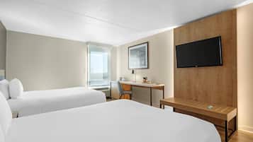 A hotel room with two beds, a desk, a chair, a TV, and a window.
