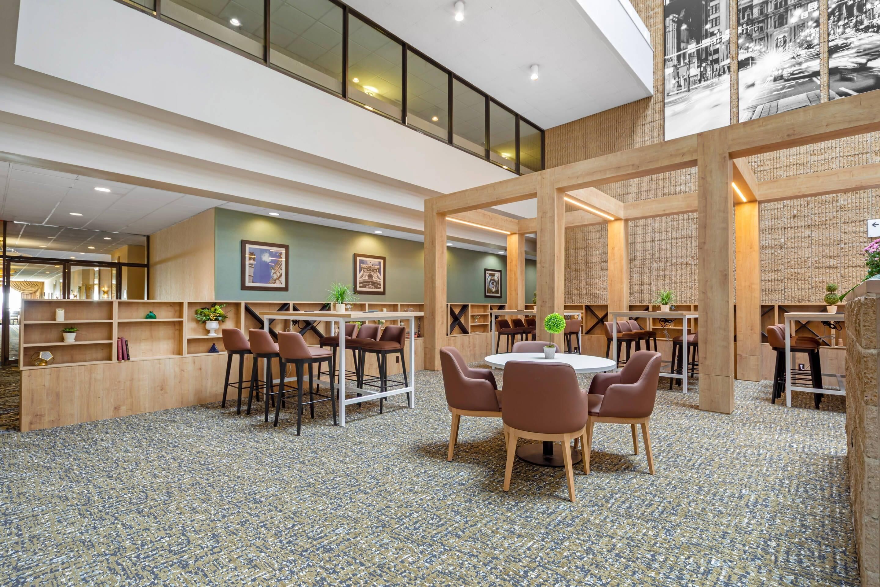 Un vaste espace intérieur aménagé avec différents types de sièges, notamment des tables rondes et des tabourets de bar, le tout entouré d’étagères en bois et de plantes en pot.