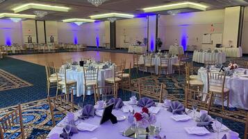 Un salón de banquetes con mesas redondas dispuestas para un evento formal, con sillas doradas, manteles blancos y centros de mesa florales.