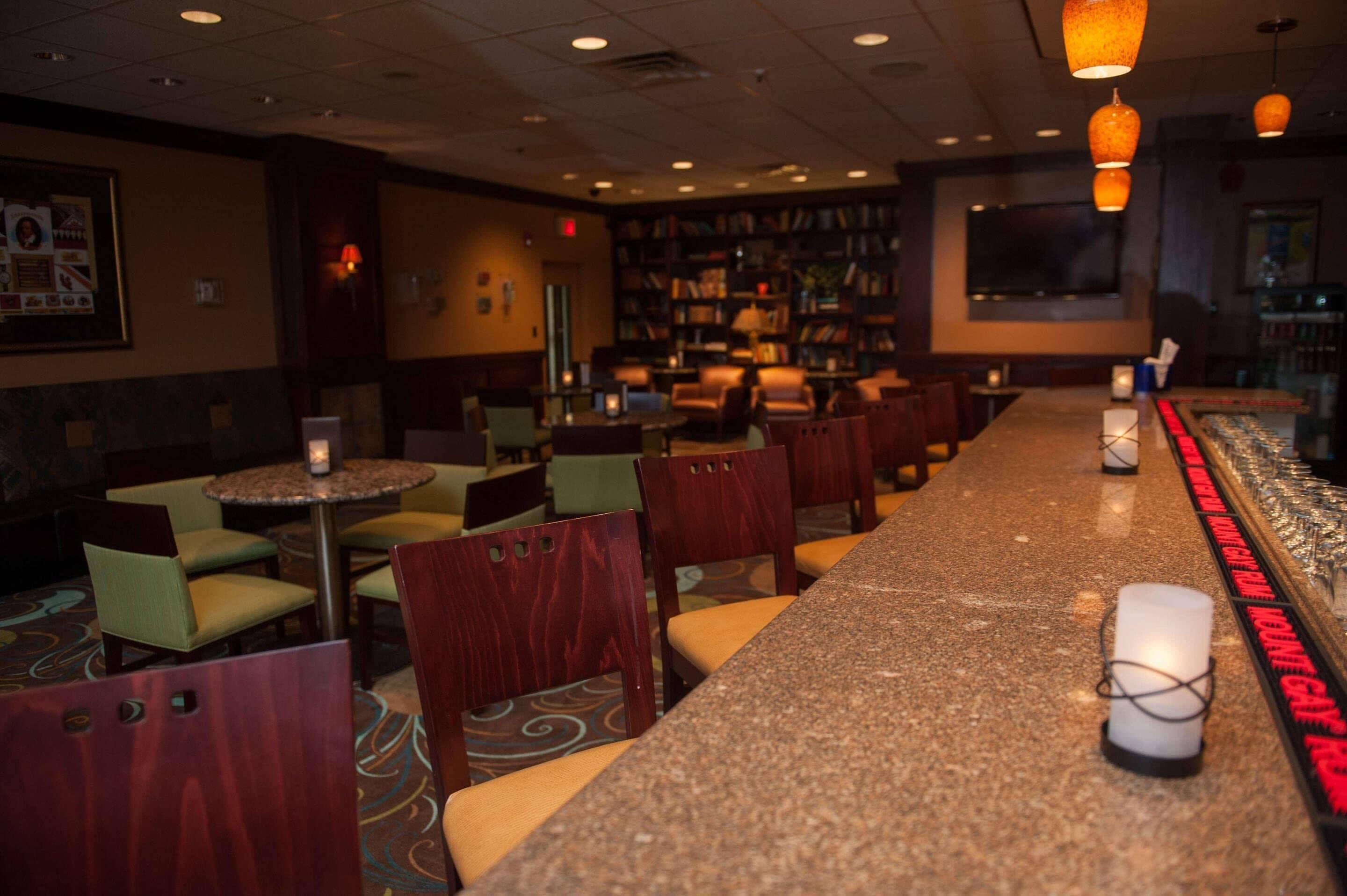 A bar area with a long counter, multiple seating options, and a bookshelf in the background.
