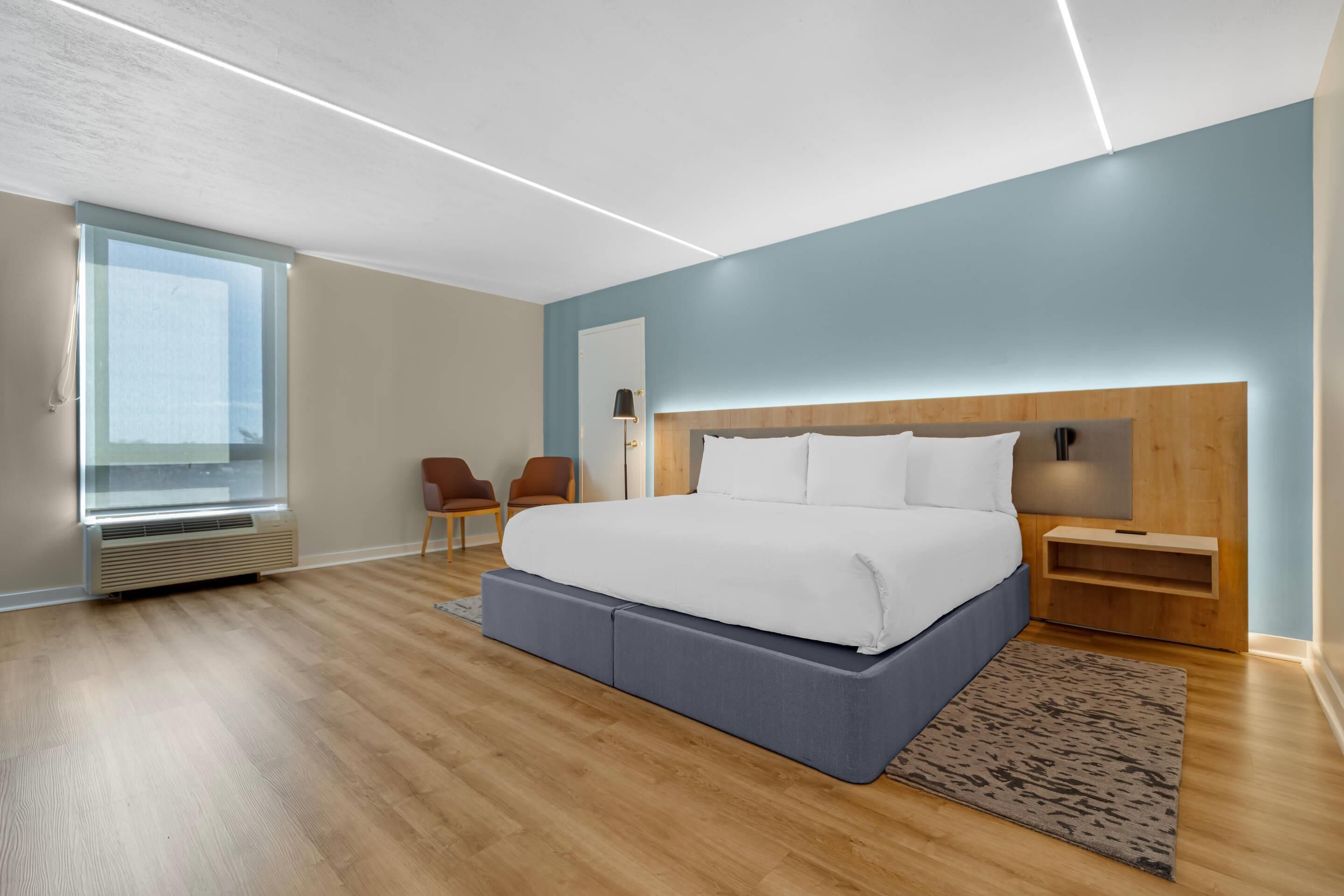 A modern bedroom with a large bed, a side table, a chair, and a window.