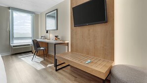 A modern room with a wooden desk, a chair, a mounted TV, and a window with a view.