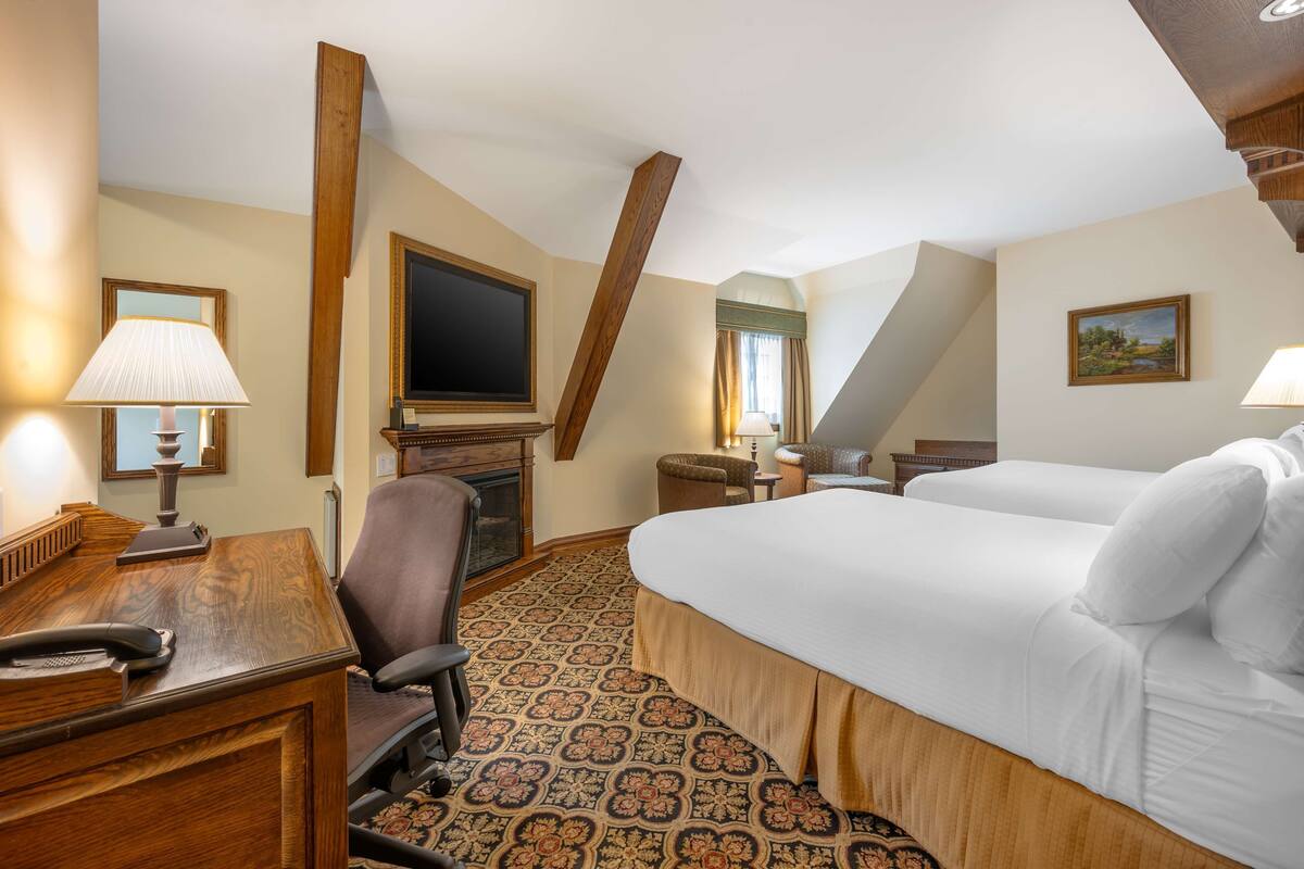 A hotel room with a large bed, a desk with a lamp, a chair, a television, and a patterned carpet.