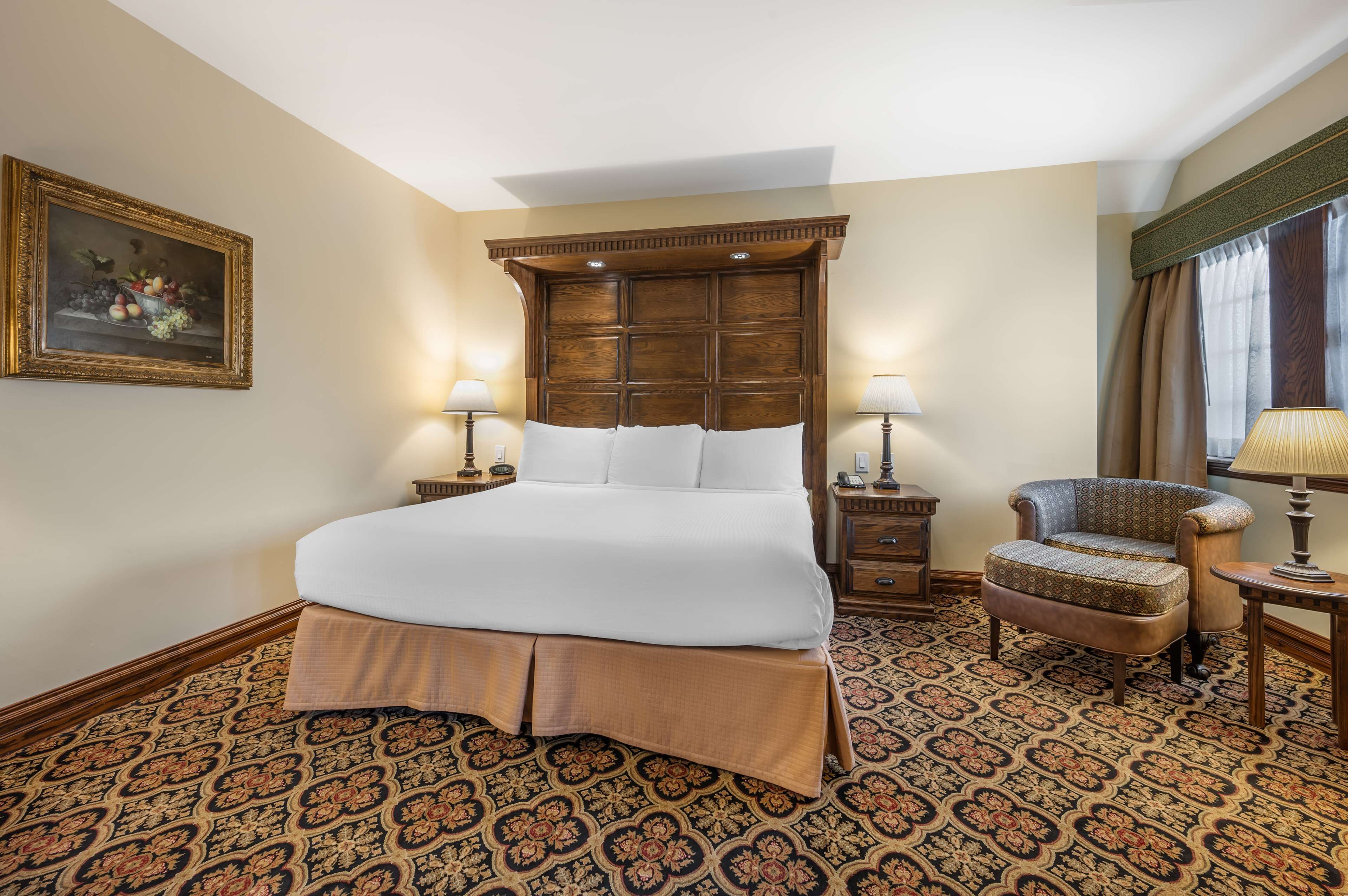 A hotel room with a large bed, two bedside tables, a chair, a patterned carpet, and a painting on the wall.