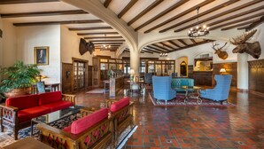 A spacious lobby with a high ceiling, wooden beams, a red sofa, blue armchairs, and a large potted plant. - Best Western Premier Mariemont Inn (Cincinnati)
