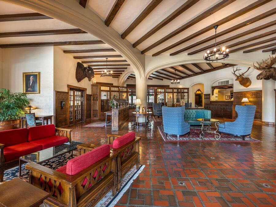 A spacious lobby with a high ceiling, wooden beams, a red sofa, blue armchairs, and a large potted plant.