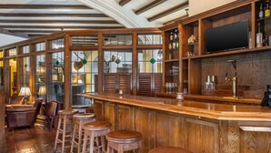 A bar area with wooden bar stools, a television mounted above the bar, and a wine rack with bottles. - Best Western Premier Mariemont Inn (Cincinnati)