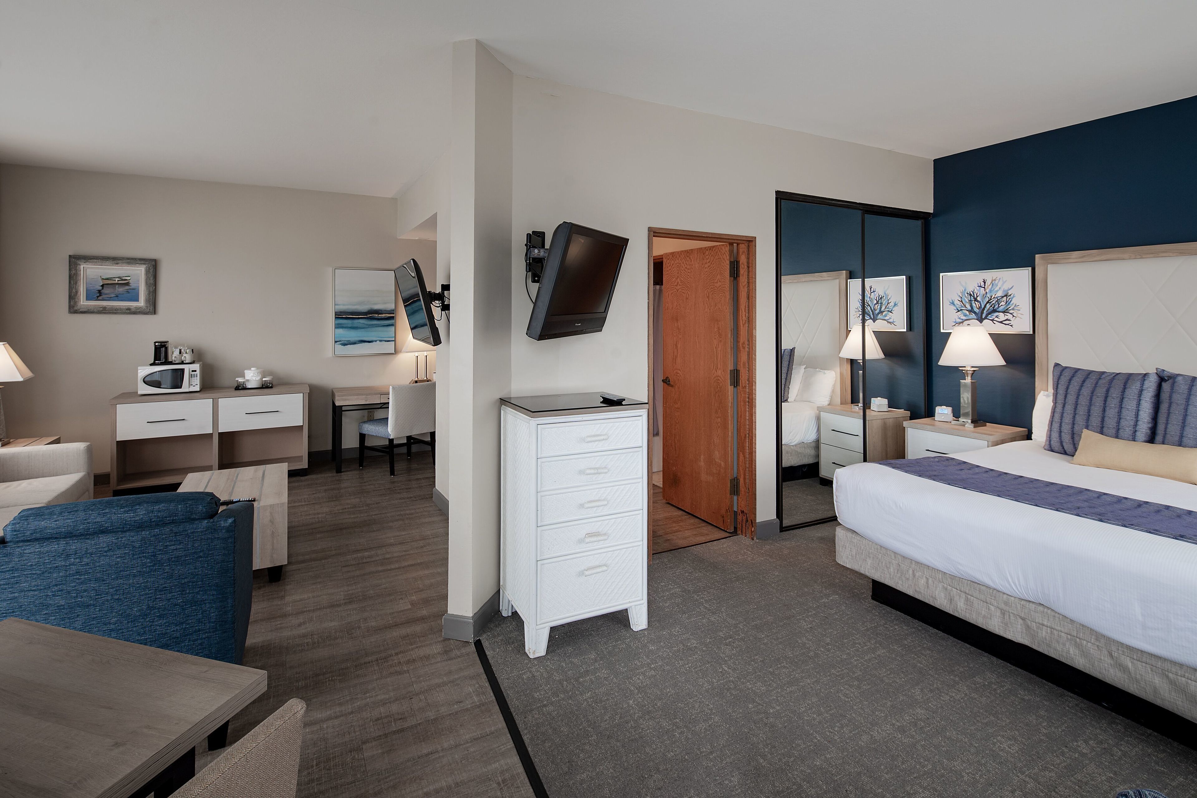 A hotel room with a bed, bedside tables, a desk, a chair, a dresser, and a television.