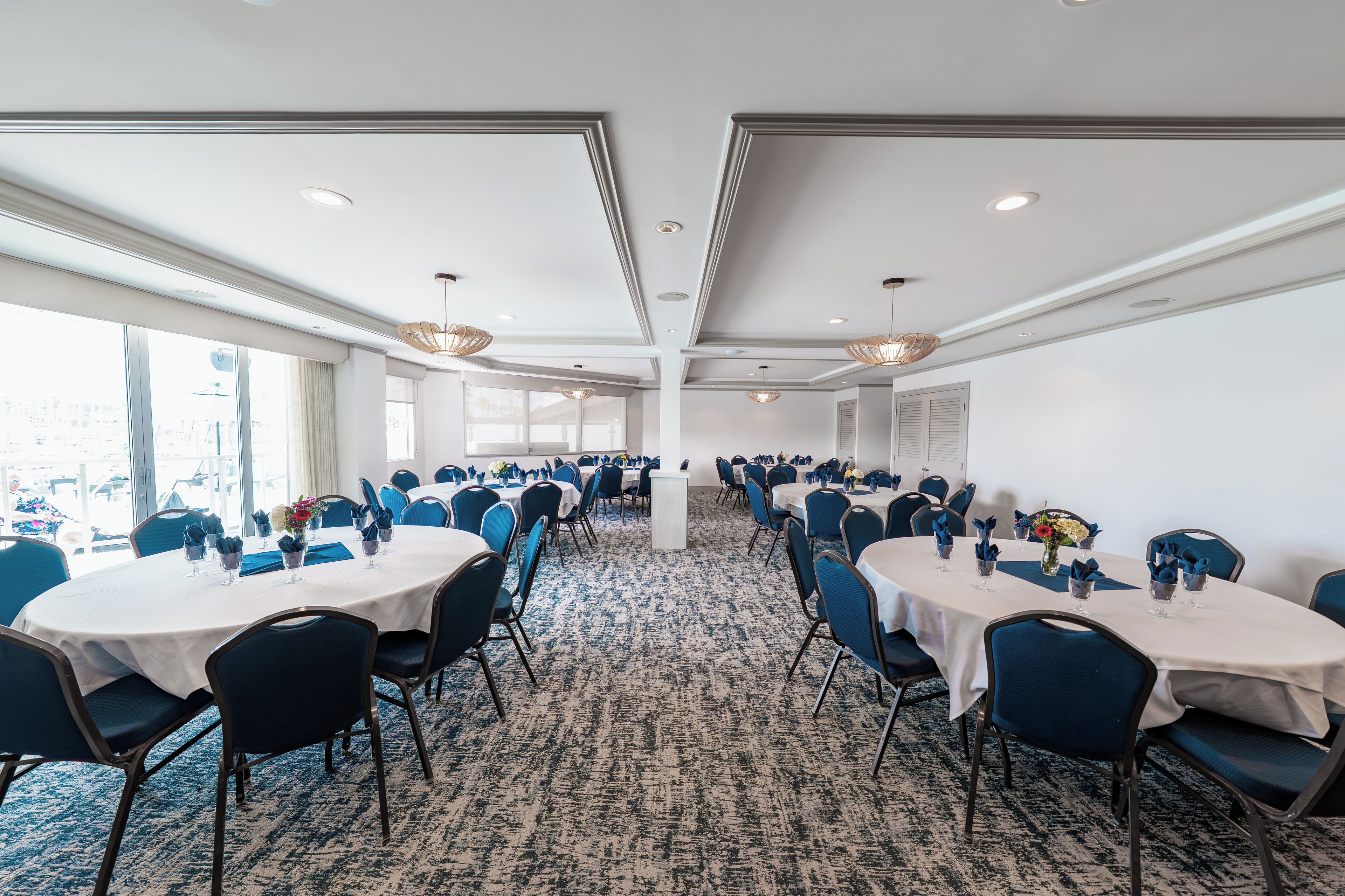 A conference room with round tables, blue chairs, and white tablecloths.
