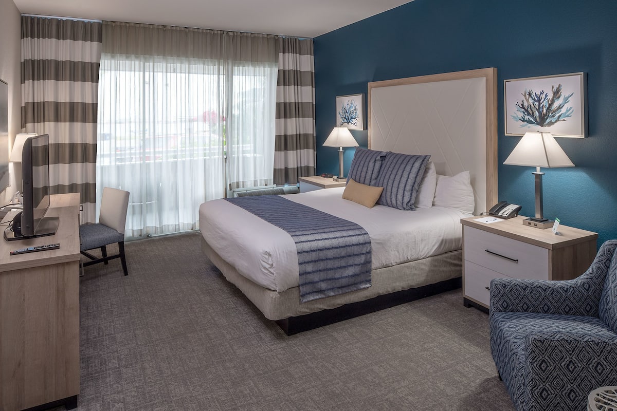 A hotel room with a large bed, two bedside tables, a desk, a chair, and a TV.