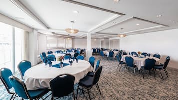 Une salle de conférence avec des tables rondes et des chaises bleues, un sol recouvert de moquette et de grandes fenêtres.