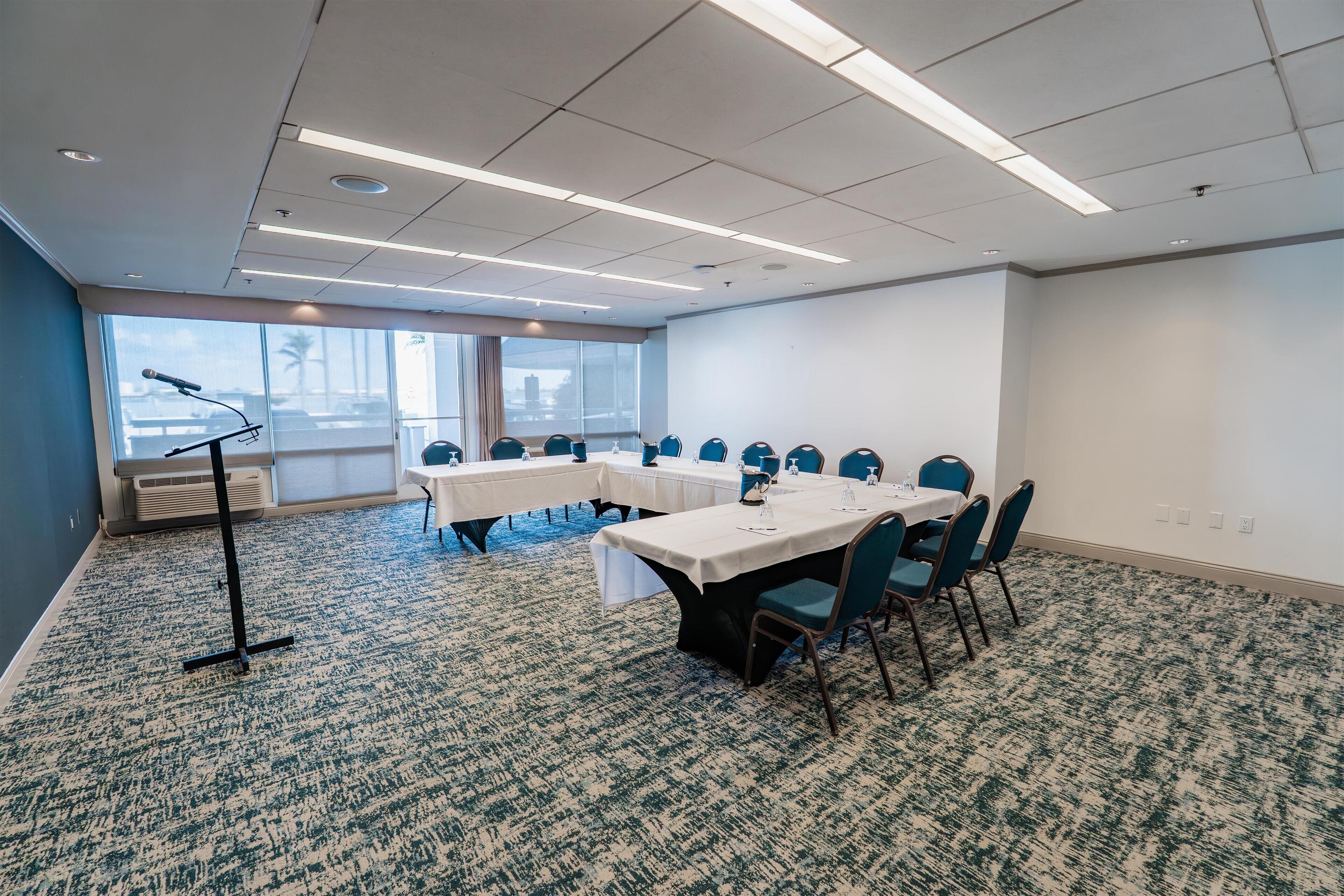 Un salón de conferencias con mesas y sillas, un atril y ventanas amplias con vistas a la ciudad.