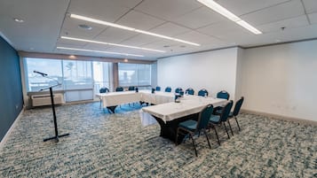 Un salón de conferencias con mesas y sillas, un atril y ventanas amplias con vistas a la ciudad.