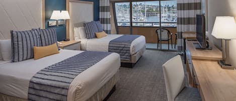 Ein Hotelzimmer mit zwei Betten, einem Schreibtisch, einem Stuhl und einem großen Fenster mit Blick auf einen Hafen.