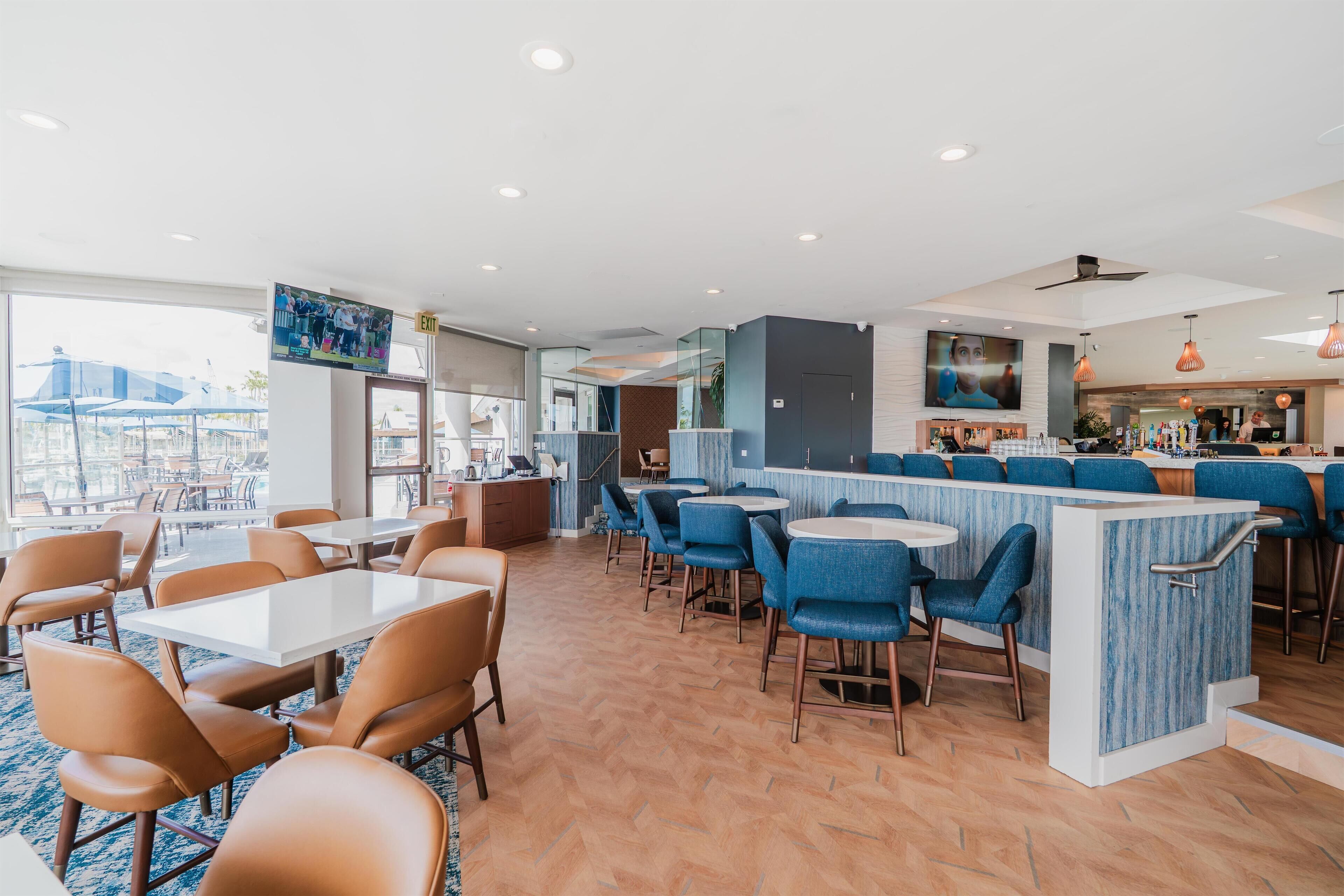 A modern restaurant with a bar area, seating arrangements, and a view of the outdoors.