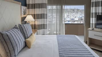 Ein Hotelzimmer mit Bett, Fernseher, Schreibtisch und Blick auf einen Yachthafen.