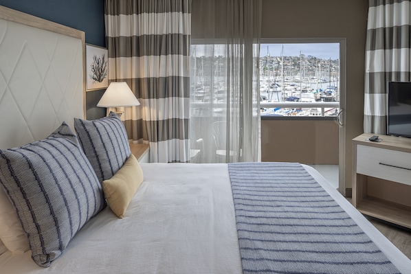 A hotel room with a bed, a TV, a desk, and a view of a marina. - Bay Club Hotel & Marina (San Diego)