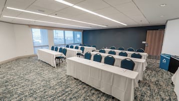 A conference room with rows of tables and chairs, a carpeted floor, and a large window with a view.