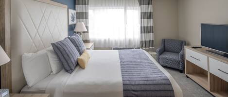 A hotel room with a large bed, a TV, a desk, and a chair.