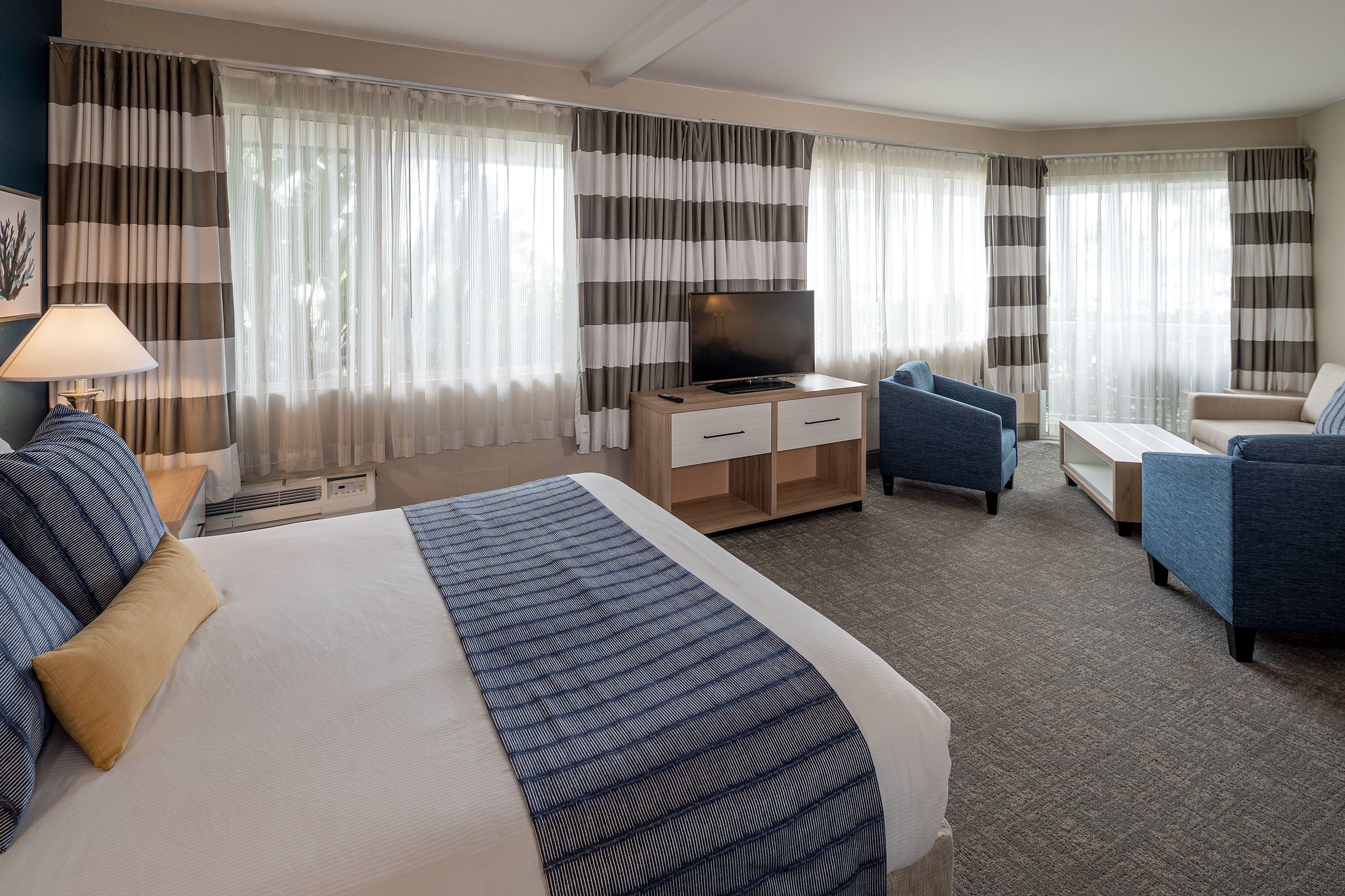 A hotel room with a bed, a desk with a TV, two armchairs, and a sofa.