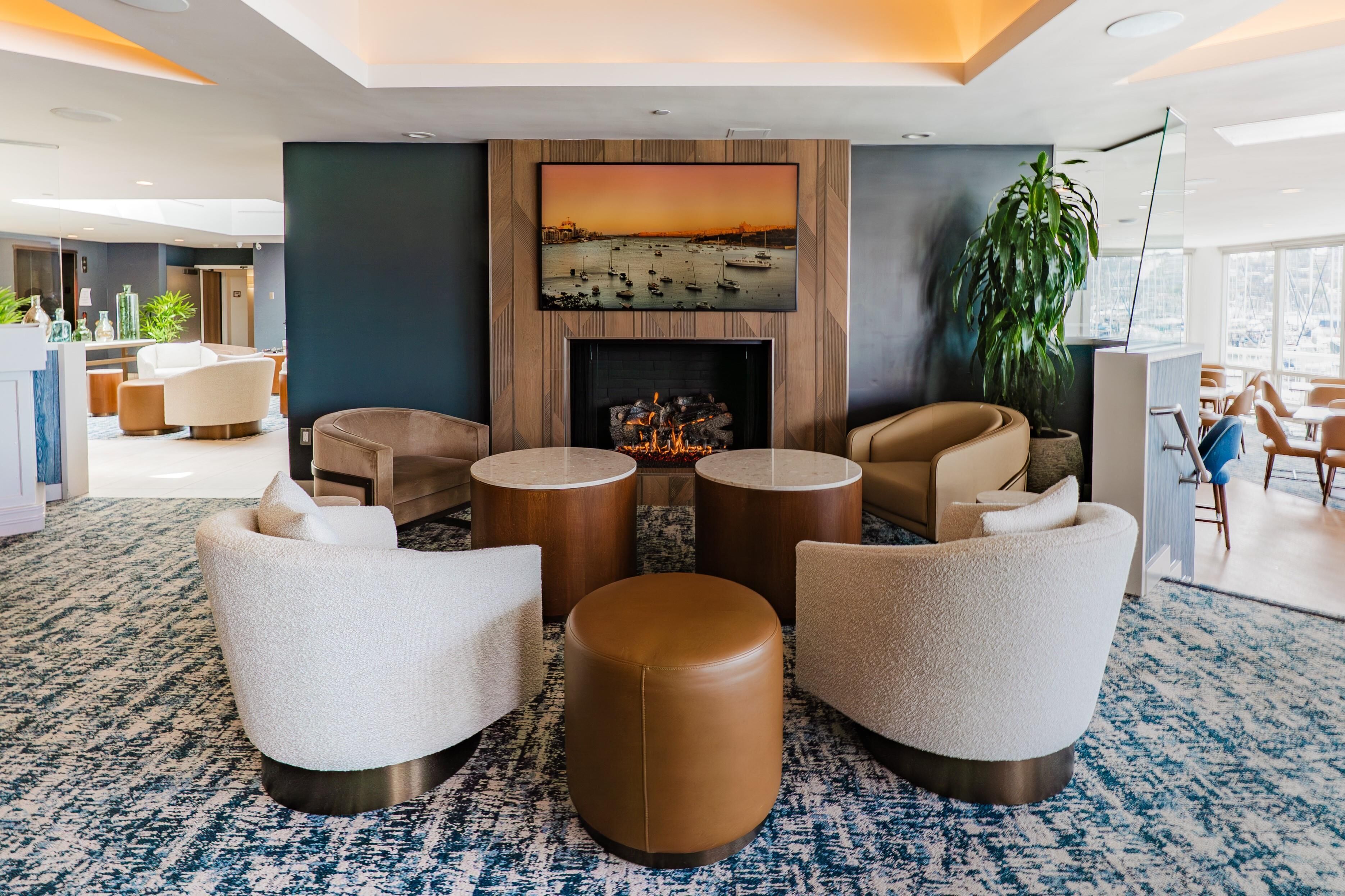 A modern lobby with a fireplace, comfortable seating, and a large painting of a sunset over water.