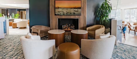 A modern lobby with a fireplace, comfortable seating, and a large painting of a sunset over water.