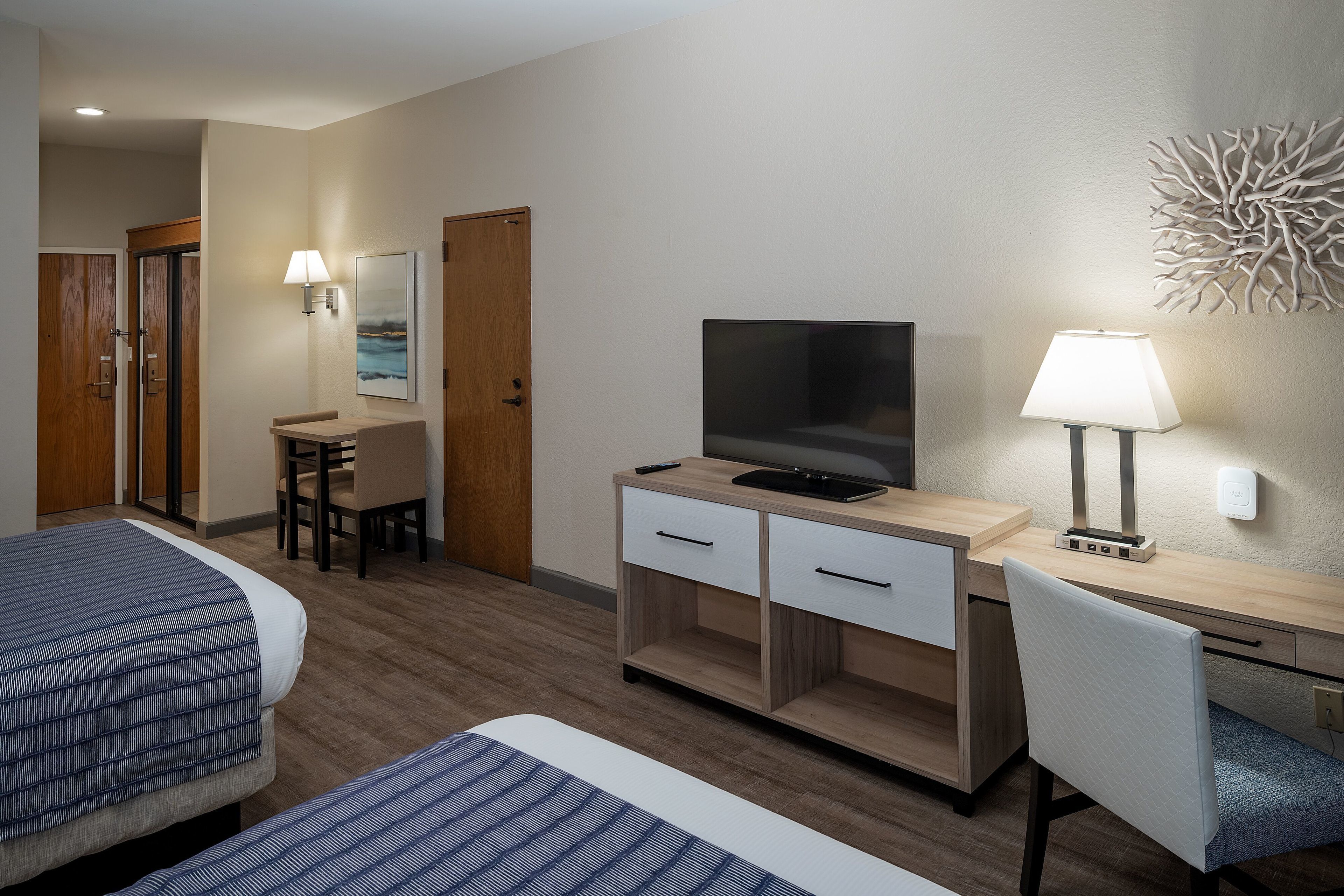 A hotel room with two beds, a desk with a TV, a chair, and a lamp.