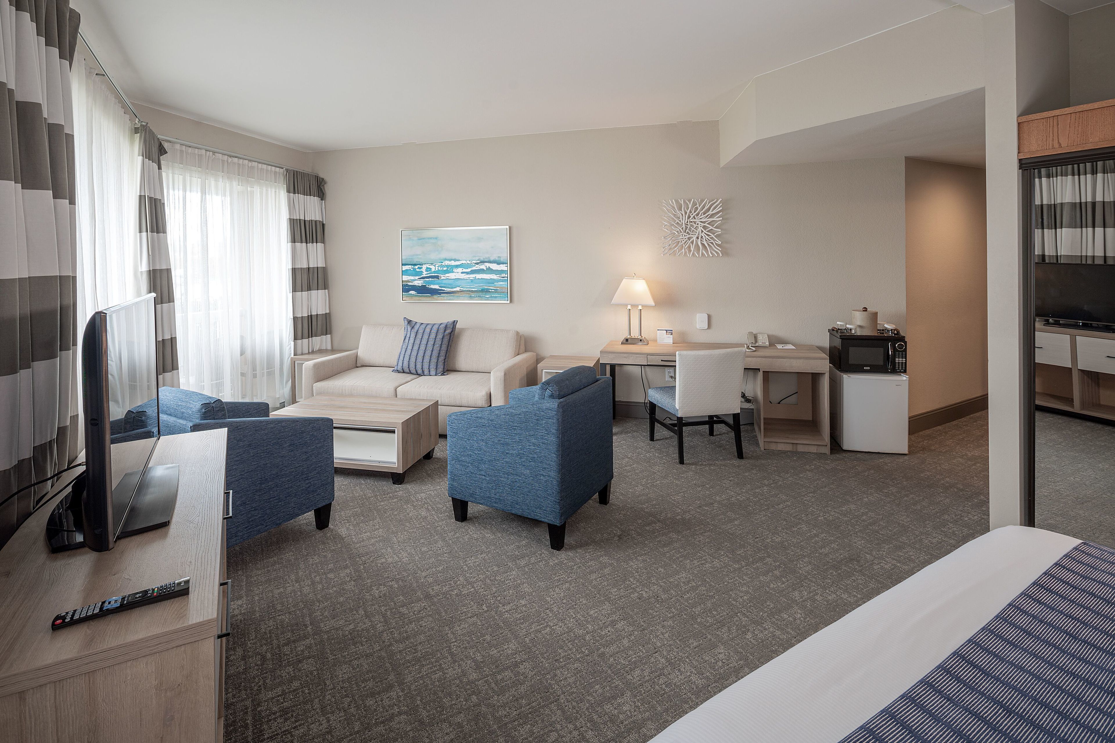 A hotel room with a bed, a desk, a chair, a sofa, and a TV.