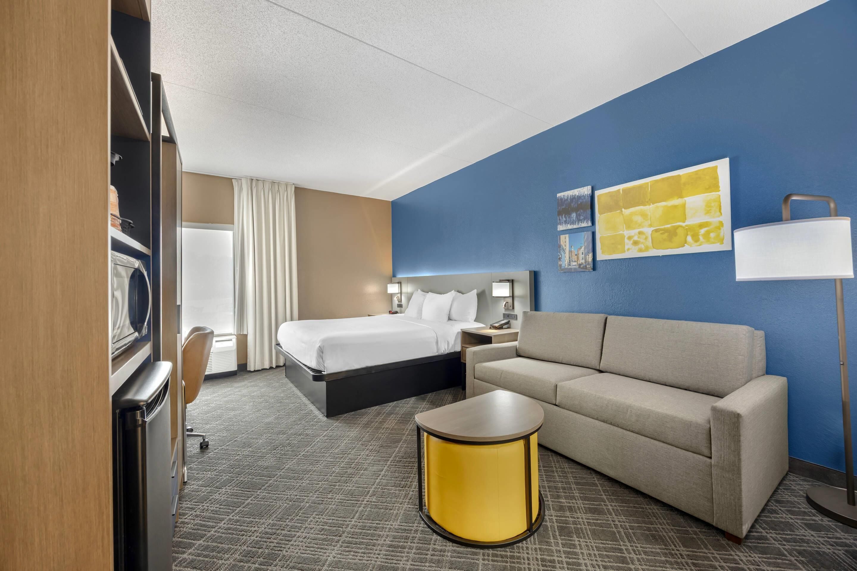 A hotel room with a bed, a sofa, a small table, and a lamp.
