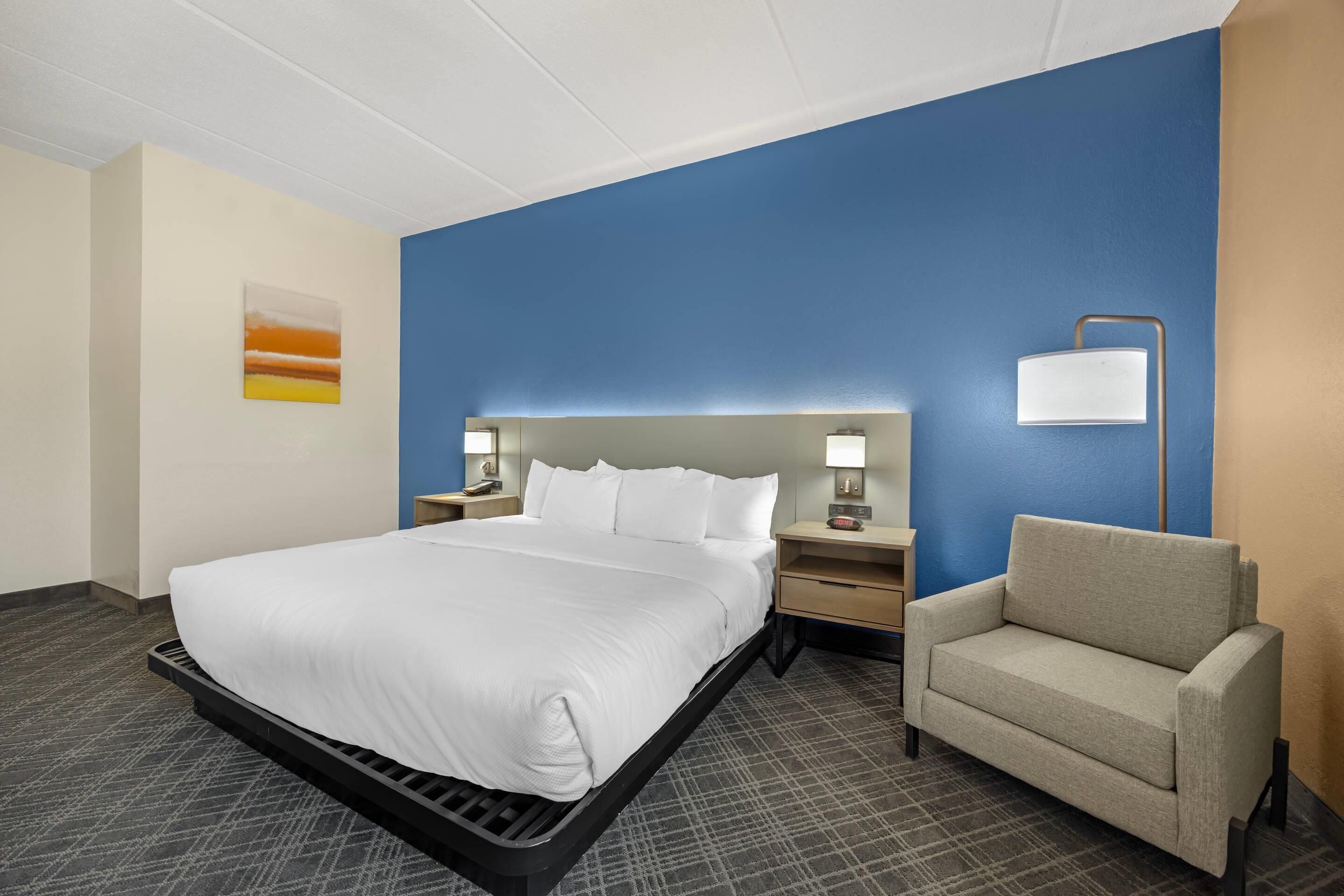A hotel room with a large bed, a nightstand with a lamp, a chair, and a painting on the wall.
