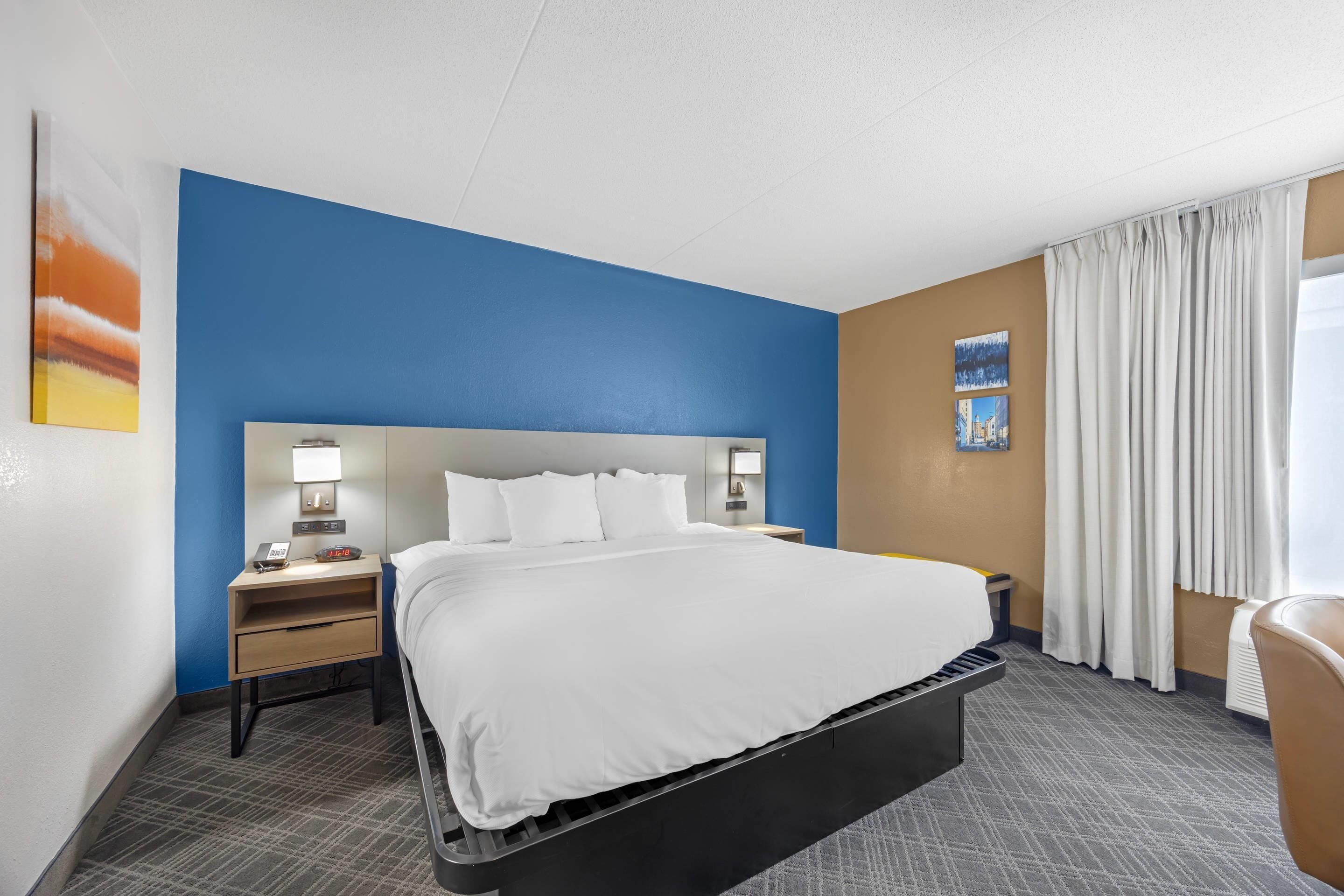 A hotel room with a bed, a nightstand, a lamp, and a window with curtains.