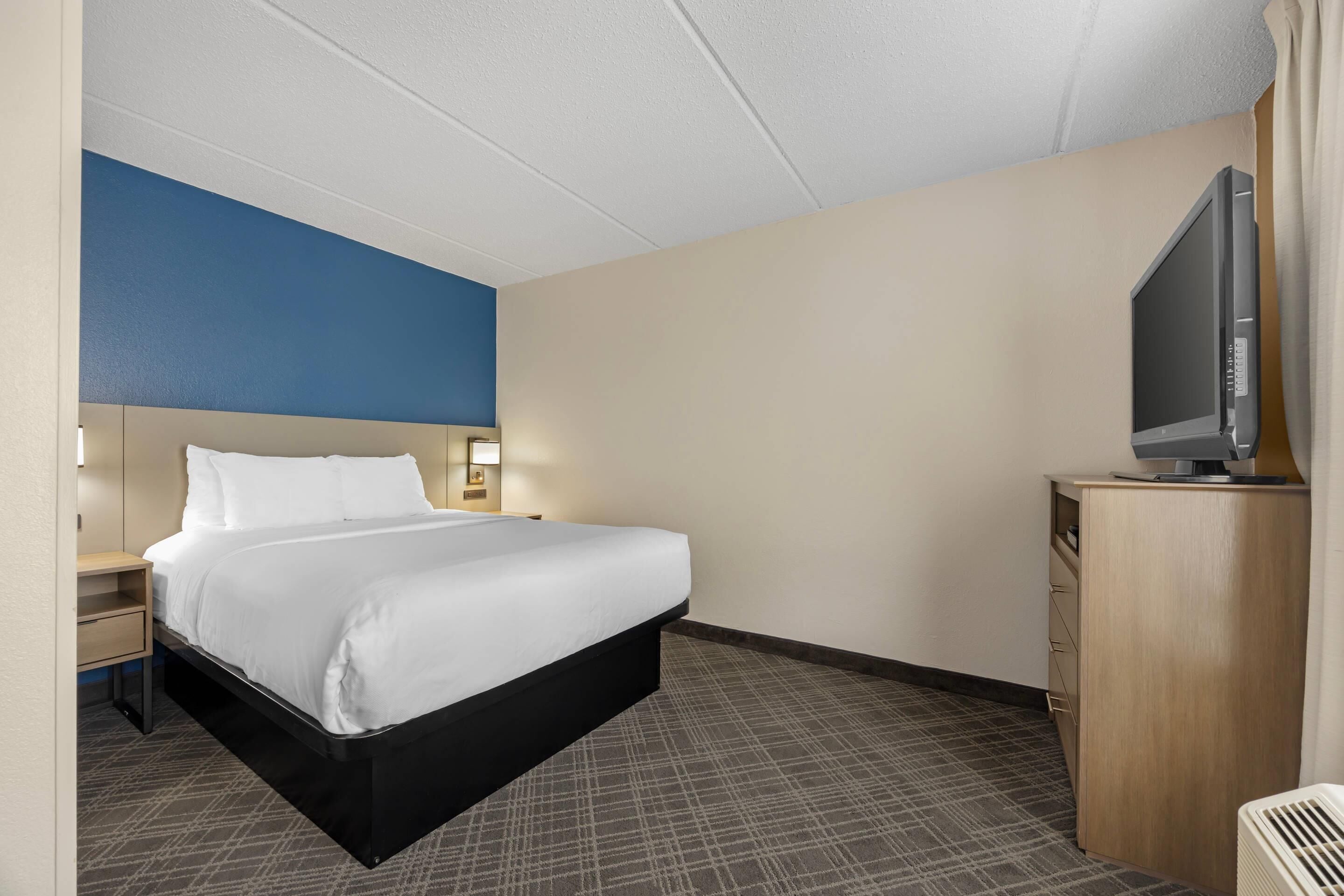 Una habitación de hotel con cama, mesita de noche, lámpara, televisor y armario.