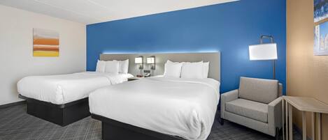 A hotel room with two beds, a desk, a chair, and a lamp.
