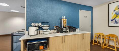 A kitchenette with a microwave, coffee maker, and bowls on a counter.